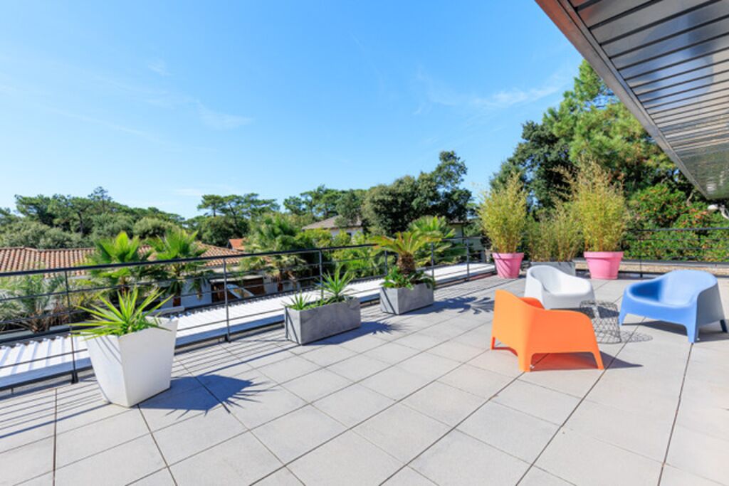 A rooftop terrace with potted plants, outdoor seating, and a clear view of the surrounding landscape.