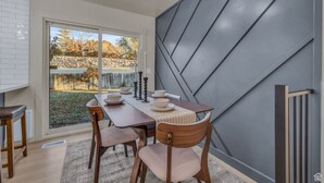 Een eetruimte met een tafel voor vier personen, zicht op een stenen muur en bomen buiten, en een modern wandontwerp.
