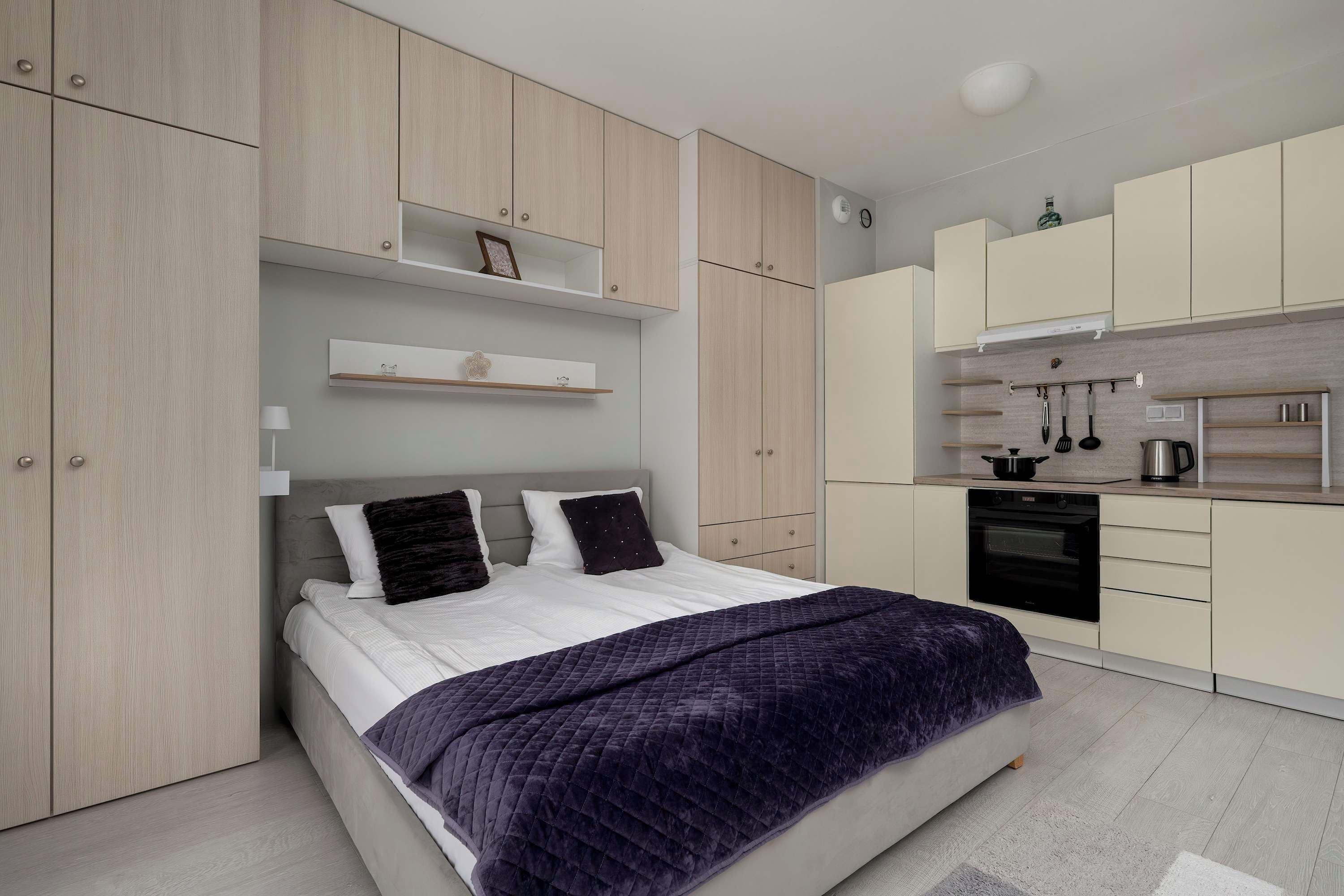 Quarto moderno com cama, armário embutido e cozinha compacta.