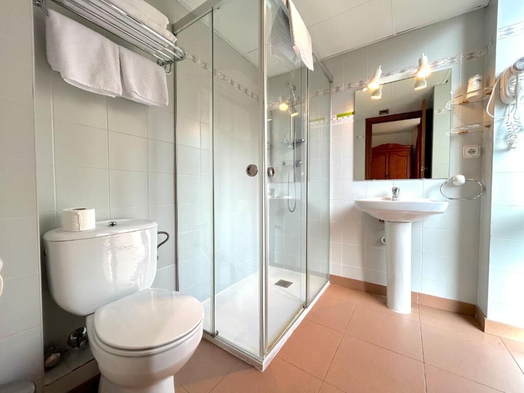 A modern bathroom with a glass-enclosed shower, a white toilet, and a sink with a mirror above it.