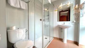 Un baño moderno con ducha acristalada, inodoro blanco y lavabo con espejo.