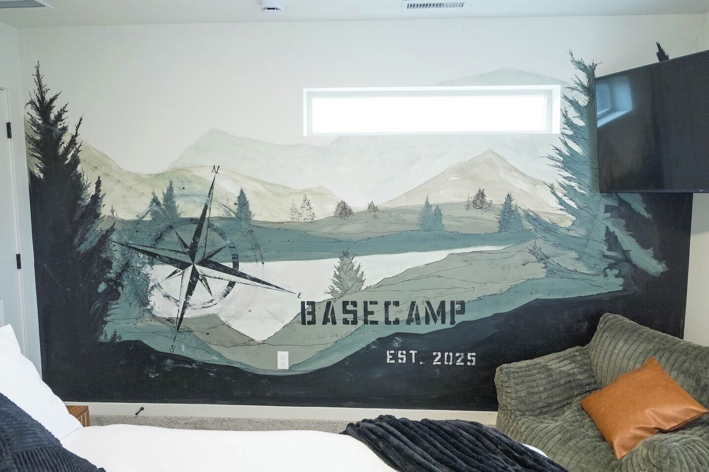 A room with a large wall mural depicting a mountainous landscape and a compass, with the text "BASE CAMP EST. 2025".