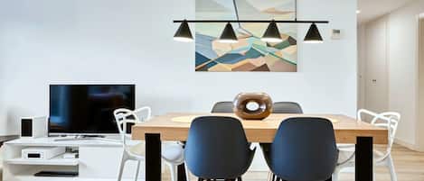 A modern dining area with a wooden table, black and white chairs, a flat-screen TV, and a geometric wall art piece.