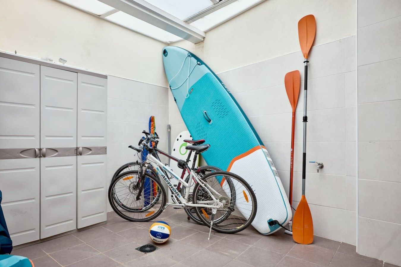 Une pièce dans laquelle on peut voir un vélo, une planche de surf et une pagaie appuyés contre le mur.