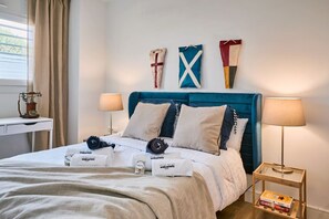 A neatly made bed with a blue headboard, two bedside lamps, and a small table with a book. - Beachfront Conquistador (El Campello)