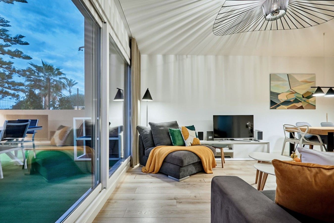 A modern living room with a large window, a sofa, a TV, and a dining area.