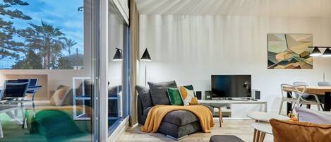 A modern living room with a large window, a sofa, a TV, and a dining area.