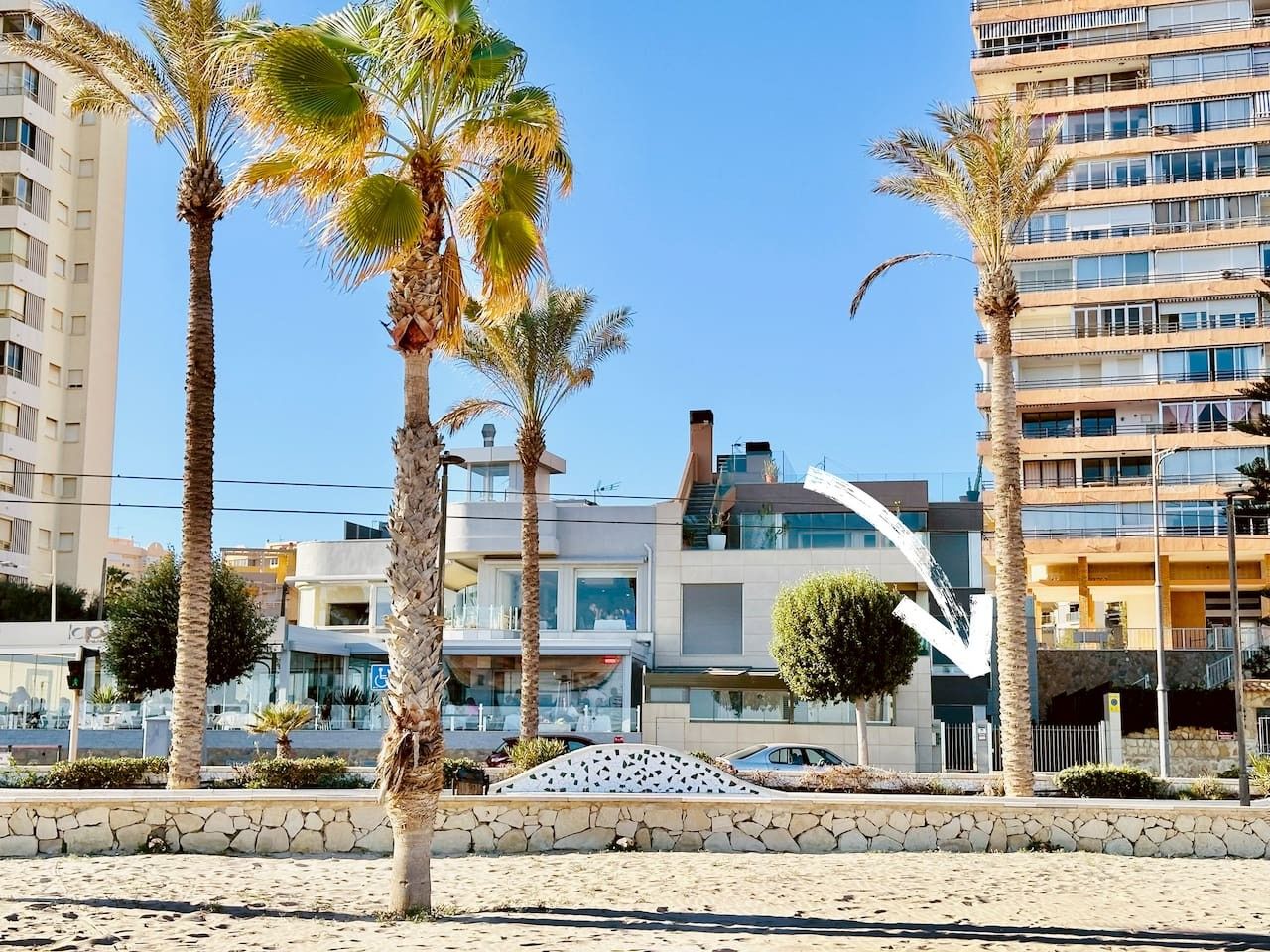 Ein Hotel direkt am Strand mit moderner Architektur, Palmen und blauem Himmel.