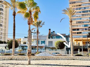 A beachfront property with modern architecture, palm trees, and a clear sky. - Beachfront Conquistador (El Campello)