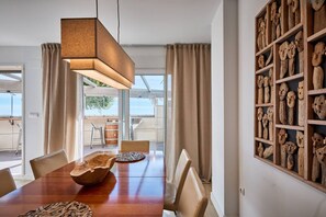 A dining area with a wooden table, chairs, a hanging light fixture, and a wall with wooden carvings. - Beachfront Conquistador (El Campello)