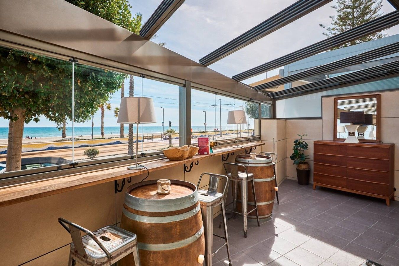 A bar area with a view of the beach, wooden bar stools, and a wooden cabinet with a mirror.
