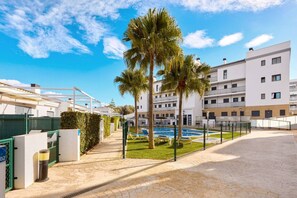 Un immeuble résidentiel doté d’une piscine, de palmiers et surplombant un ciel dégagé.