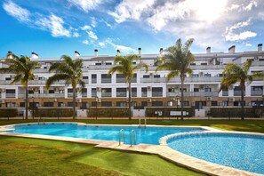 A hotel with a swimming pool, palm trees, and a clear sky. - Las Dunas 215 (Oliva)