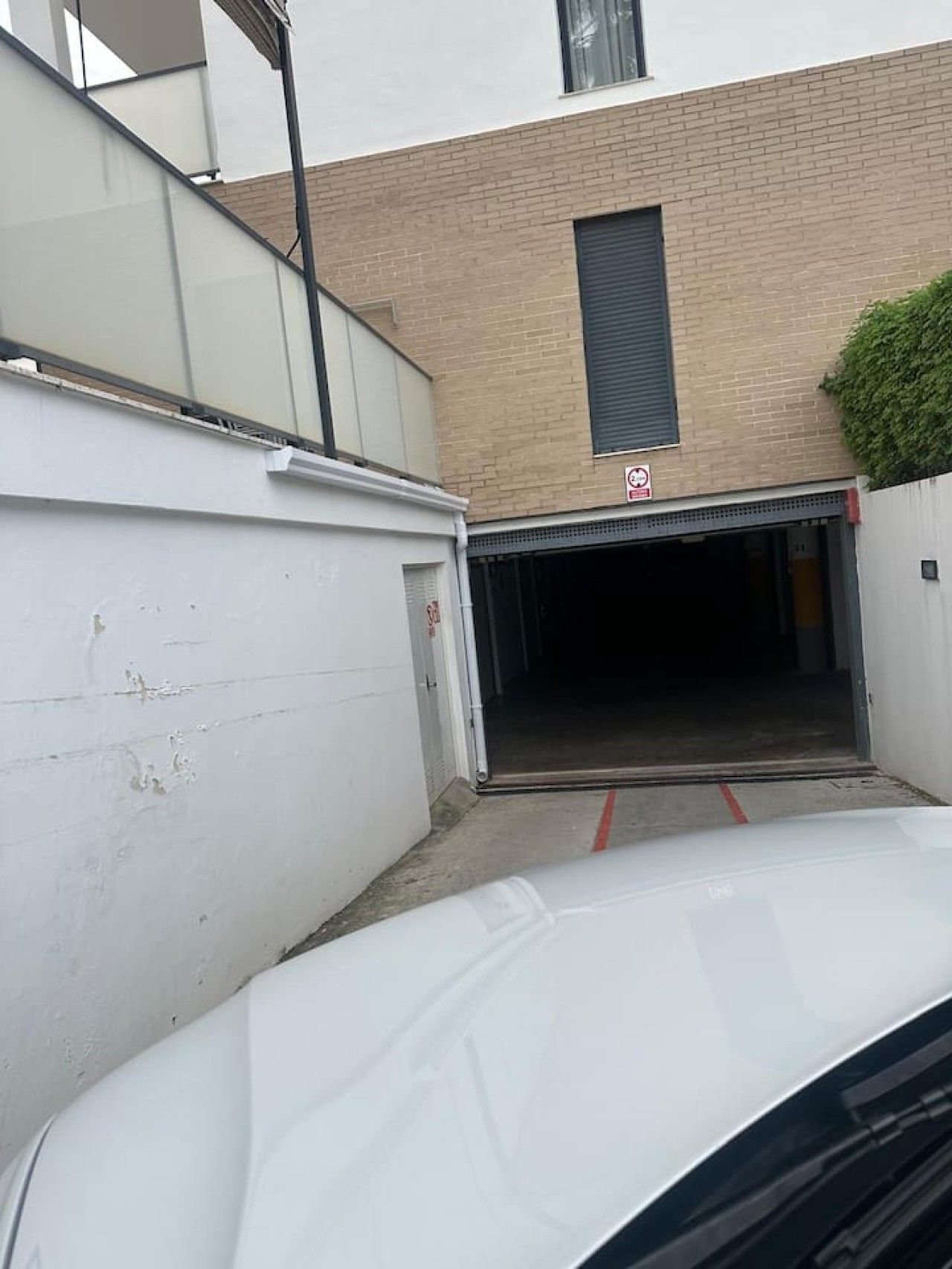 Ein weißes Auto parkt in einer schmalen Auffahrt, die zu einer Garage mit einem 'No Parking'-Schild führt.