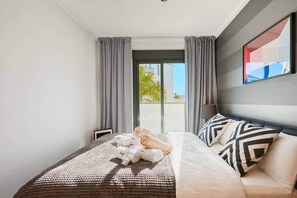 A modern hotel room with a large bed, grey curtains, a view of the outdoors, and a framed artwork on the wall. - Las Dunas 515 (Oliva)