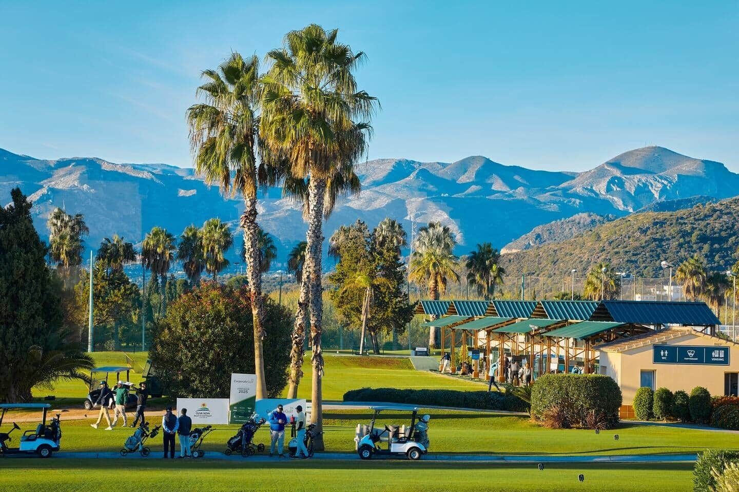 A golf course with palm trees, a clubhouse, and mountains in the background.