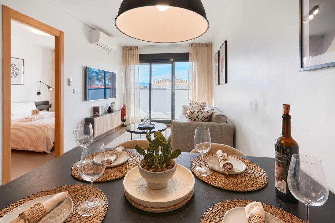 Un coin repas avec une table dressée pour deux personnes, une plante en pot et une bouteille de vin.