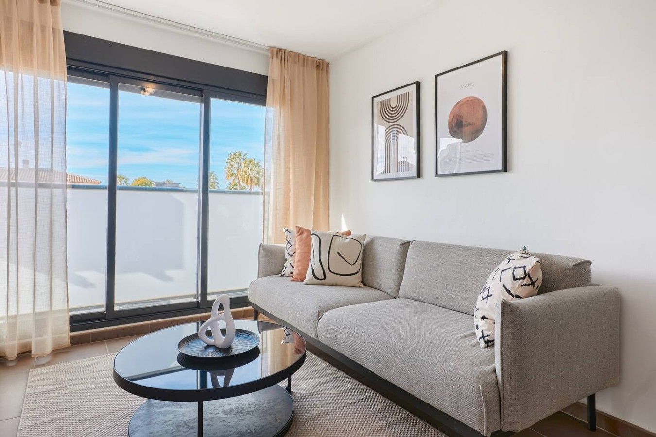 A modern living room with a grey sofa, a round glass coffee table, and two framed pictures on the wall.