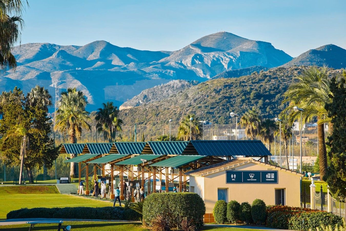 A golf course with a clubhouse, solar panels, and a mountainous backdrop.