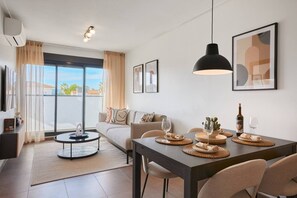 A modern living room with a dining area, large windows, and a view of the outdoors. - Las Dunas 214 (Oliva)