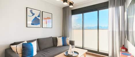 A modern living room with a grey sofa, a wooden coffee table, and a large window with curtains.