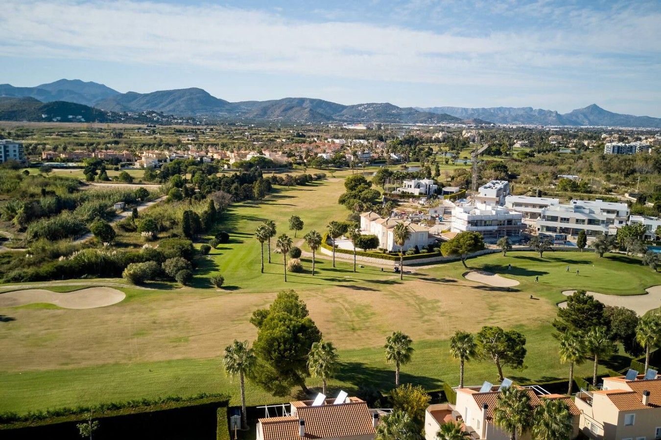A golf course with a clubhouse, palm trees, and a mountainous backdrop.
