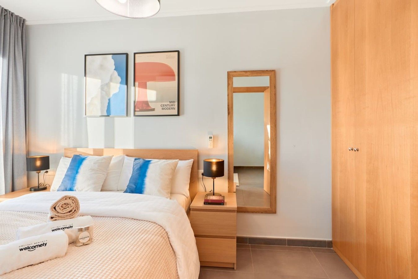 A hotel room with a bed, bedside lamps, a nightstand, a mirror, and artwork on the wall.