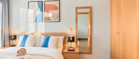 A hotel room with a bed, bedside lamps, a nightstand, a mirror, and artwork on the wall.