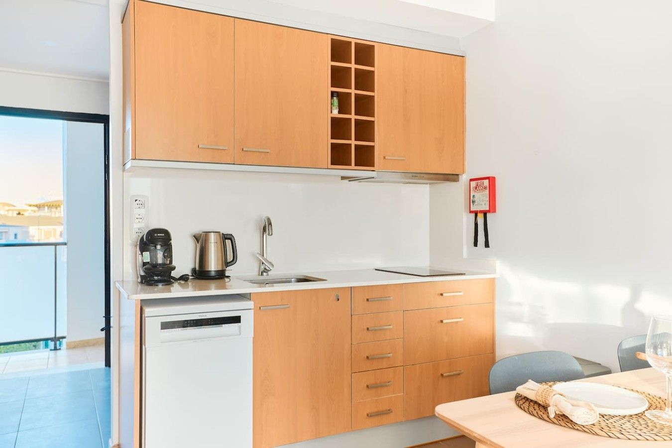 A compact kitchen with wooden cabinets, a dishwasher, a coffee maker, and a kettle.