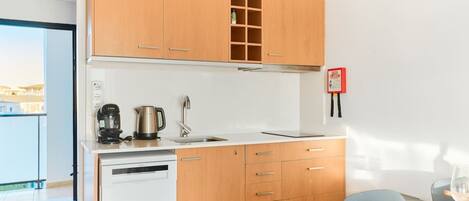 Una cocina compacta con armarios de madera, lavavajillas, cafetera y hervidor.