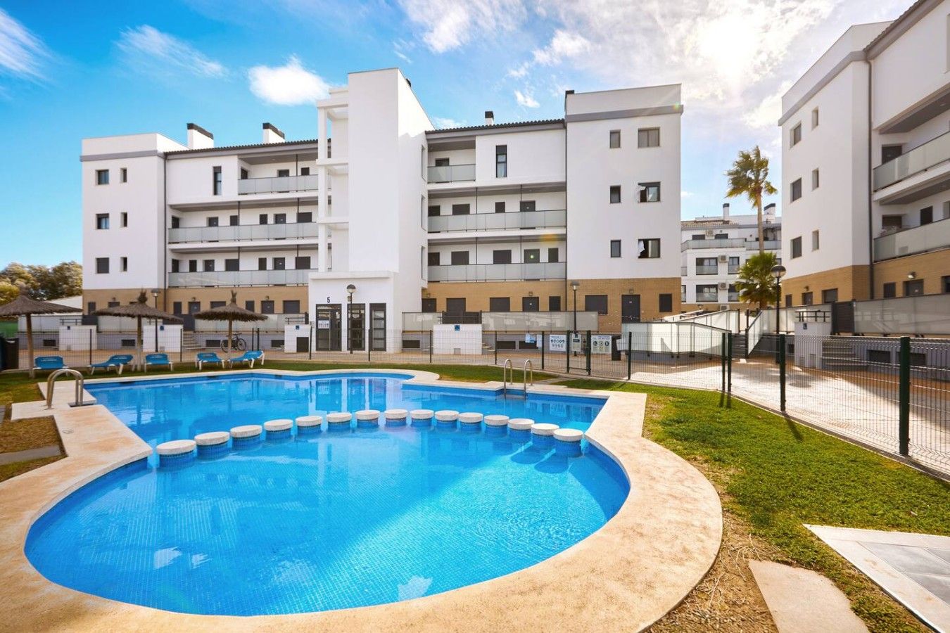 A modern hotel with a central swimming pool, multiple balconies, and a well-maintained lawn area.