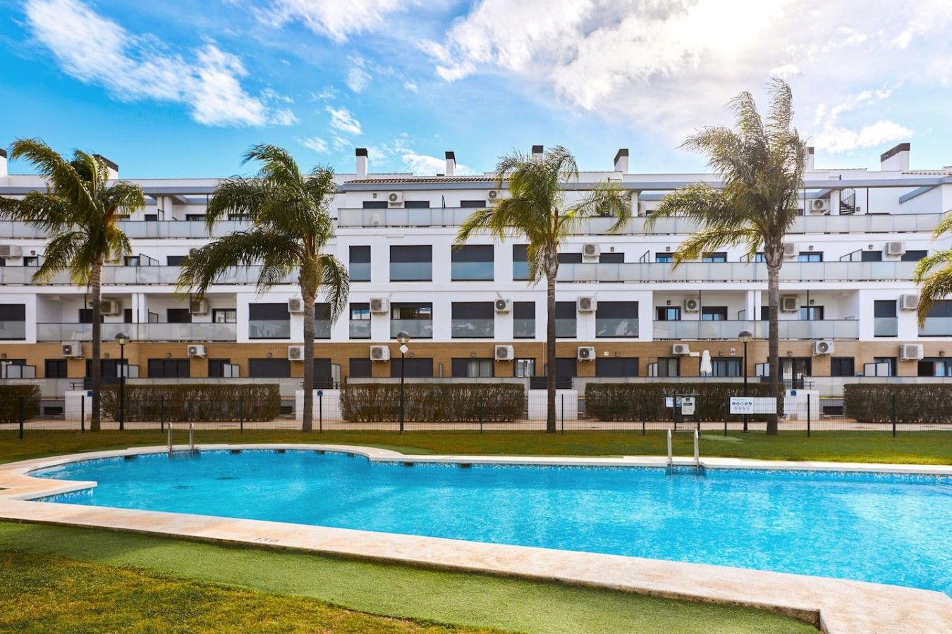Un hôtel moderne doté d’une piscine, de palmiers et surplombant un ciel d’un bleu éclatant.
