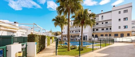 Un edificio residencial con piscina, palmeras y cielo despejado.