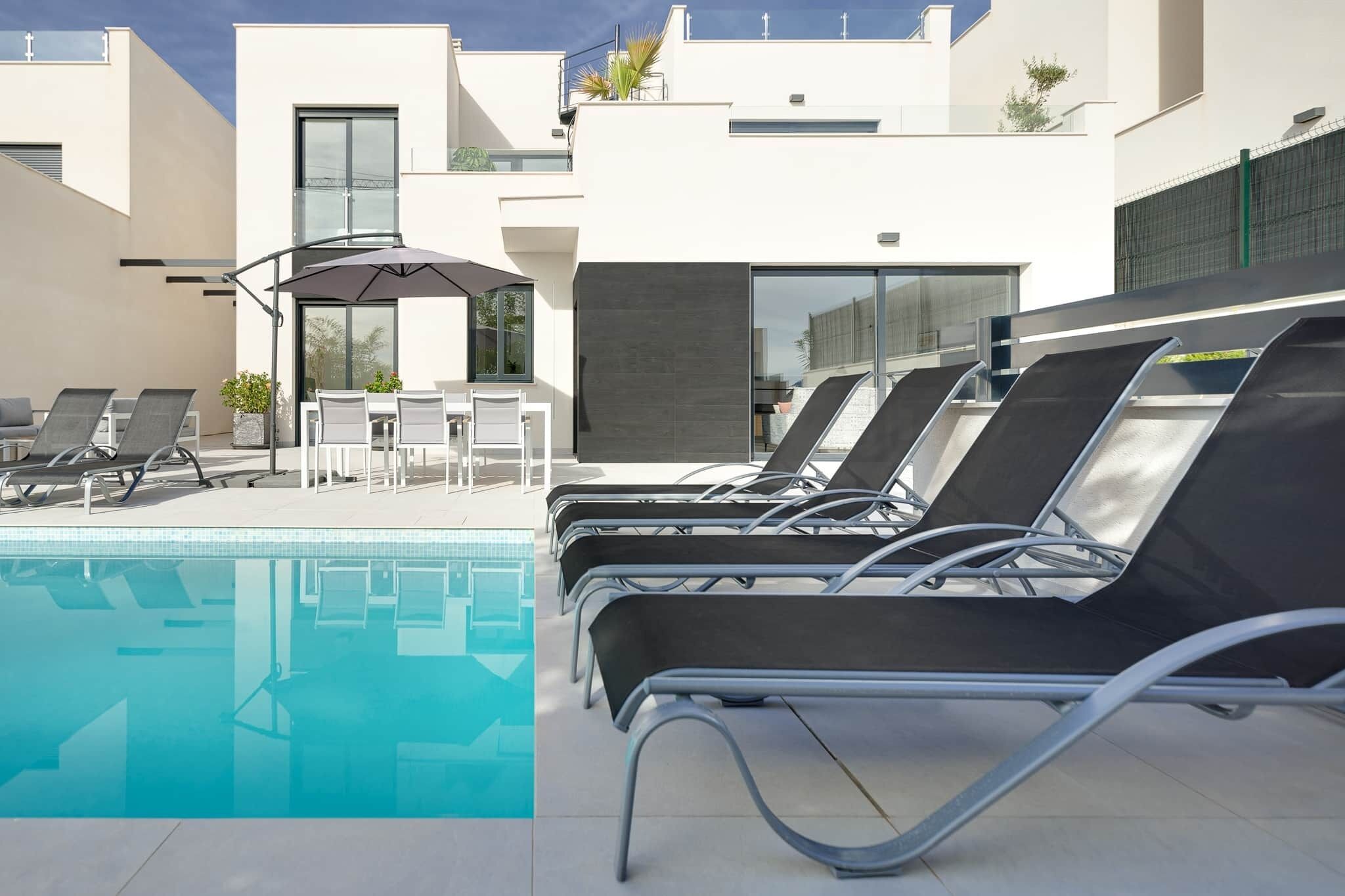 A modern outdoor pool area with lounge chairs and a covered seating area.
