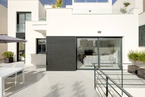 A modern outdoor patio with a glass door leading to a living area, a white outdoor seating area, and potted plants. - Polop Luxury Villa (Barony of Polop)