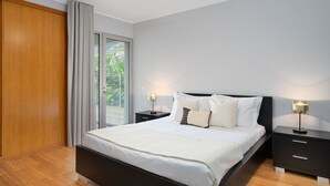 A modern bedroom with a large bed, two bedside tables with lamps, a ceiling fan, and a sliding glass door to the outside. - Anchored in Carmo by Homie (Camara de Lobos)