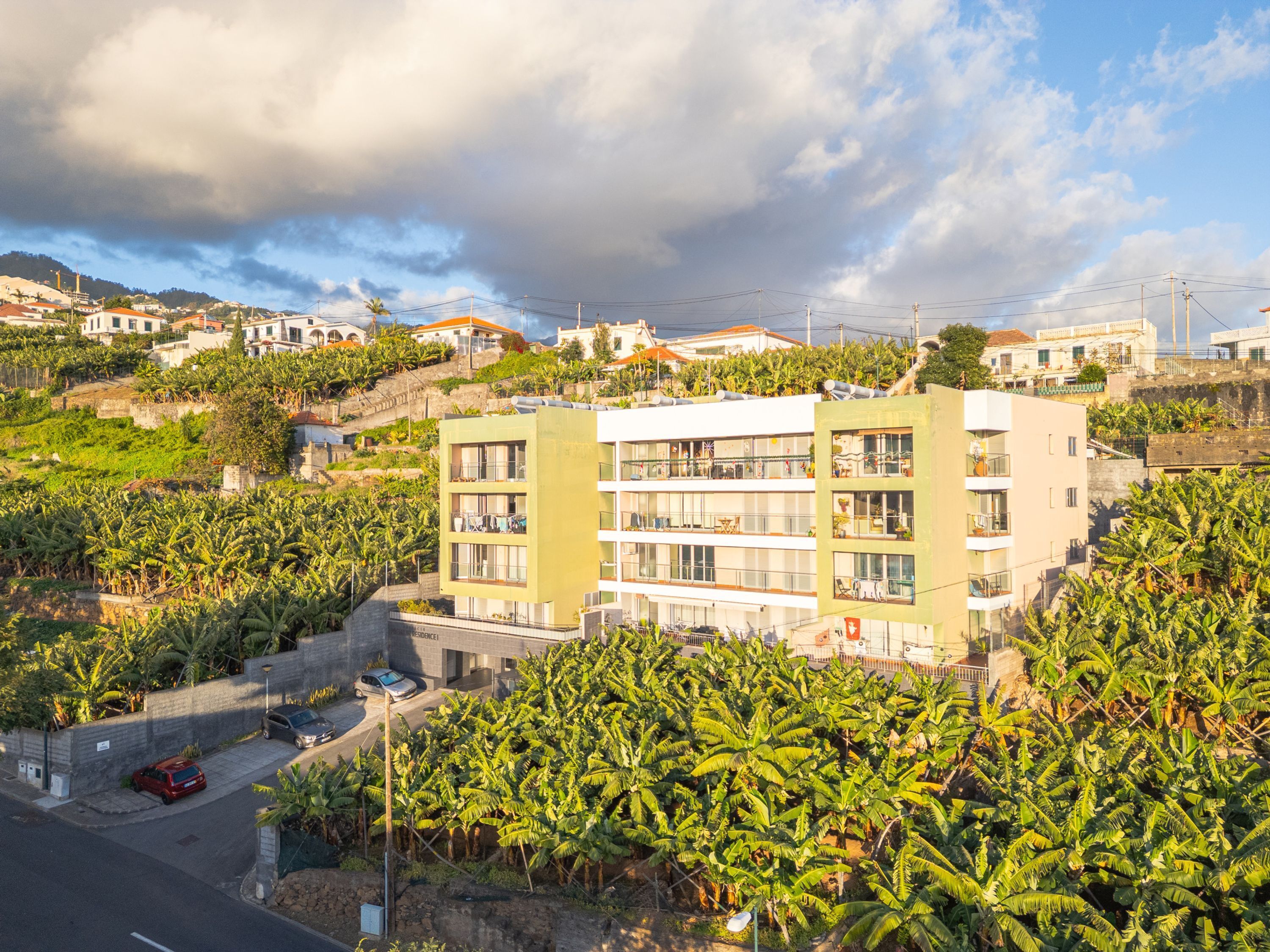 A multi-story building with balconies, surrounded by lush banana plants.