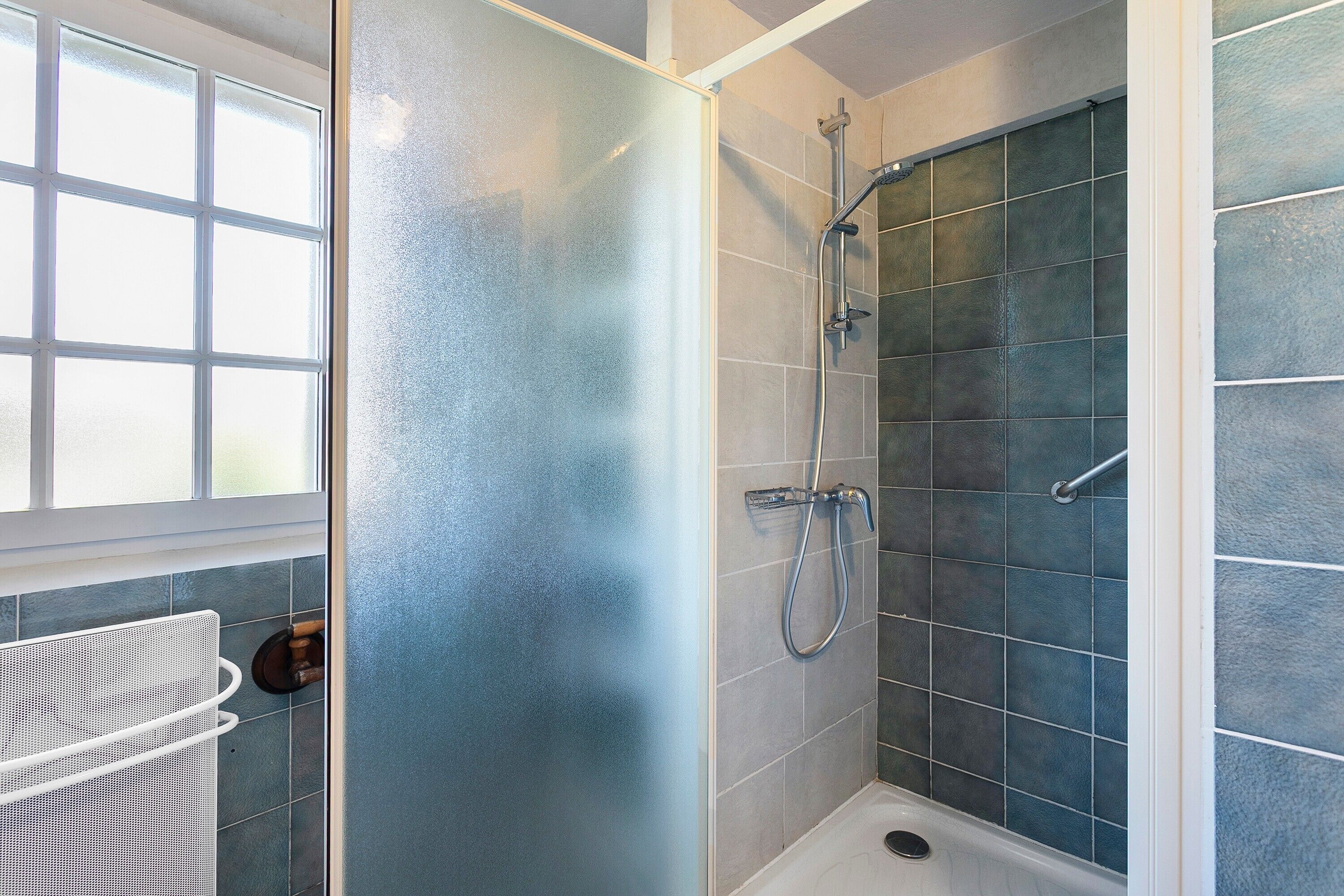A shower with a glass door, a metal showerhead, and a white bathtub.