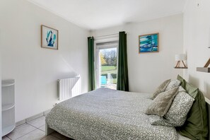 Una camera da letto con un letto, un termosifone, una finestra con tende e due quadri appesi al muro.