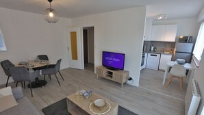 Ein modernes Wohnzimmer mit Essbereich, einer Küche und einem Fernseher, der ein Programm zeigt.