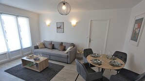 Ein modernes Wohnzimmer mit einem grauen Sofa, einem Holztisch und einem Essbereich mit einem runden Tisch und schwarzen Stühlen.