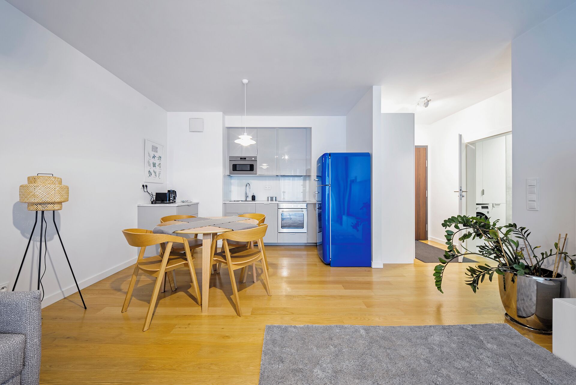 A modern kitchen with white cabinets, a blue refrigerator, and a dining area with wooden chairs and a table.