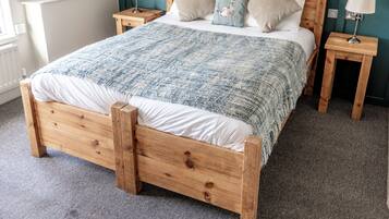 Una cama de madera con colcha azul y blanca, dos mesitas de noche con lámparas y un cabecero color turquesa.