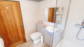 A bathroom with a wooden door, a white toilet, a sink, and a glass shower enclosure.