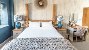 Un dormitorio con cabecera de madera, una cama grande con ropa blanca, dos mesitas de noche con lámparas, un escritorio con una silla y un espejo.