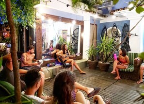 An outdoor seating area with people sitting and socializing, surrounded by potted plants and a wooden deck. - Aurora Hostel Rio (Rio de Janeiro)