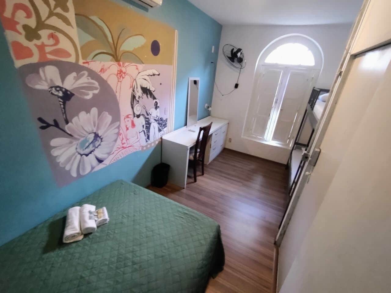 A compact room with a bed, a desk, and a chair. There is a window with a view of the outside.