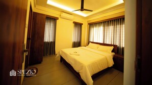 Un dormitorio amplio con una cama grande, un ventilador de techo y cortinas en las ventanas.