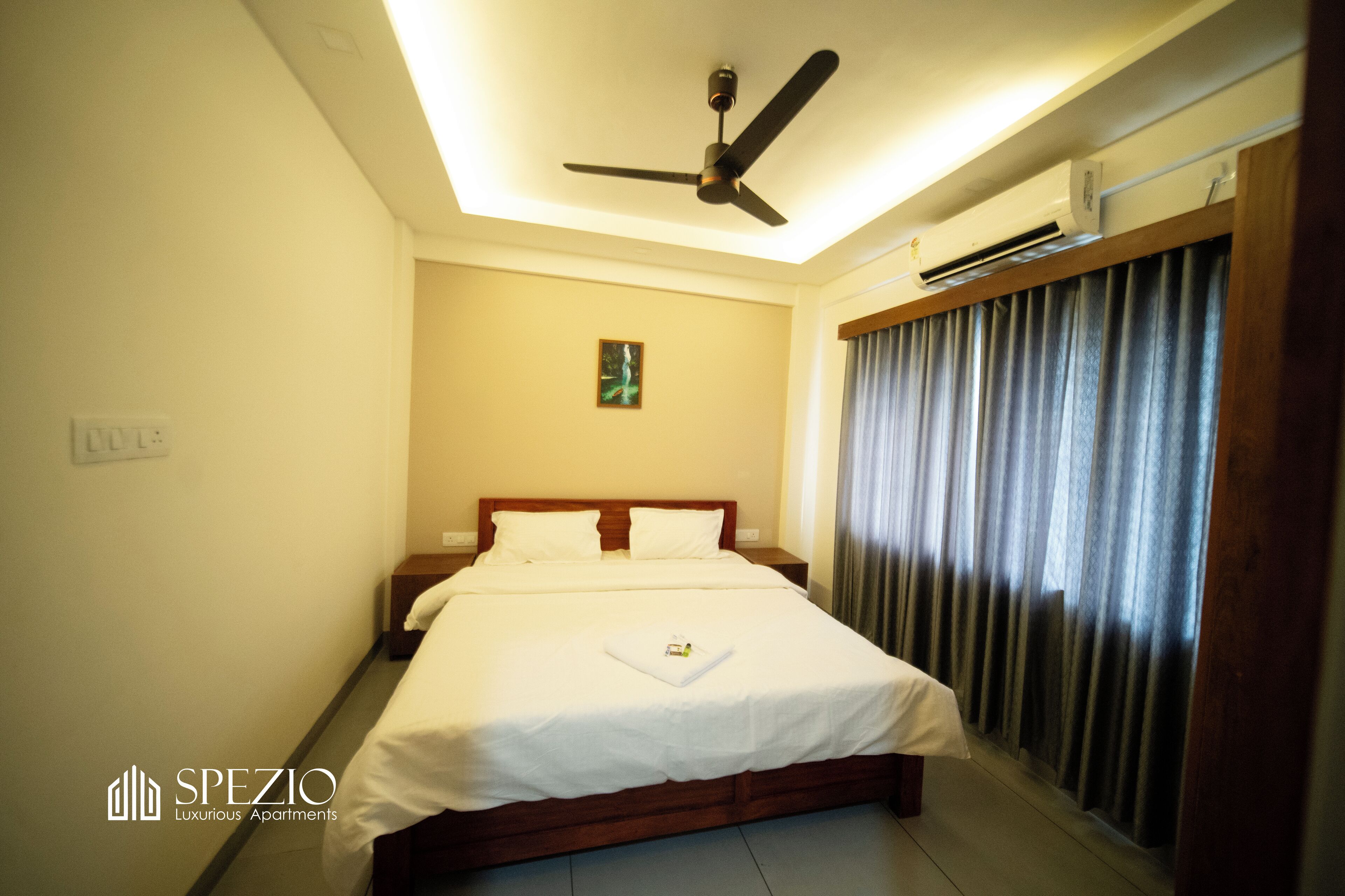 Habitación de hotel con cama, ventilador de techo, equipo de aire acondicionado y ventana con cortinas.