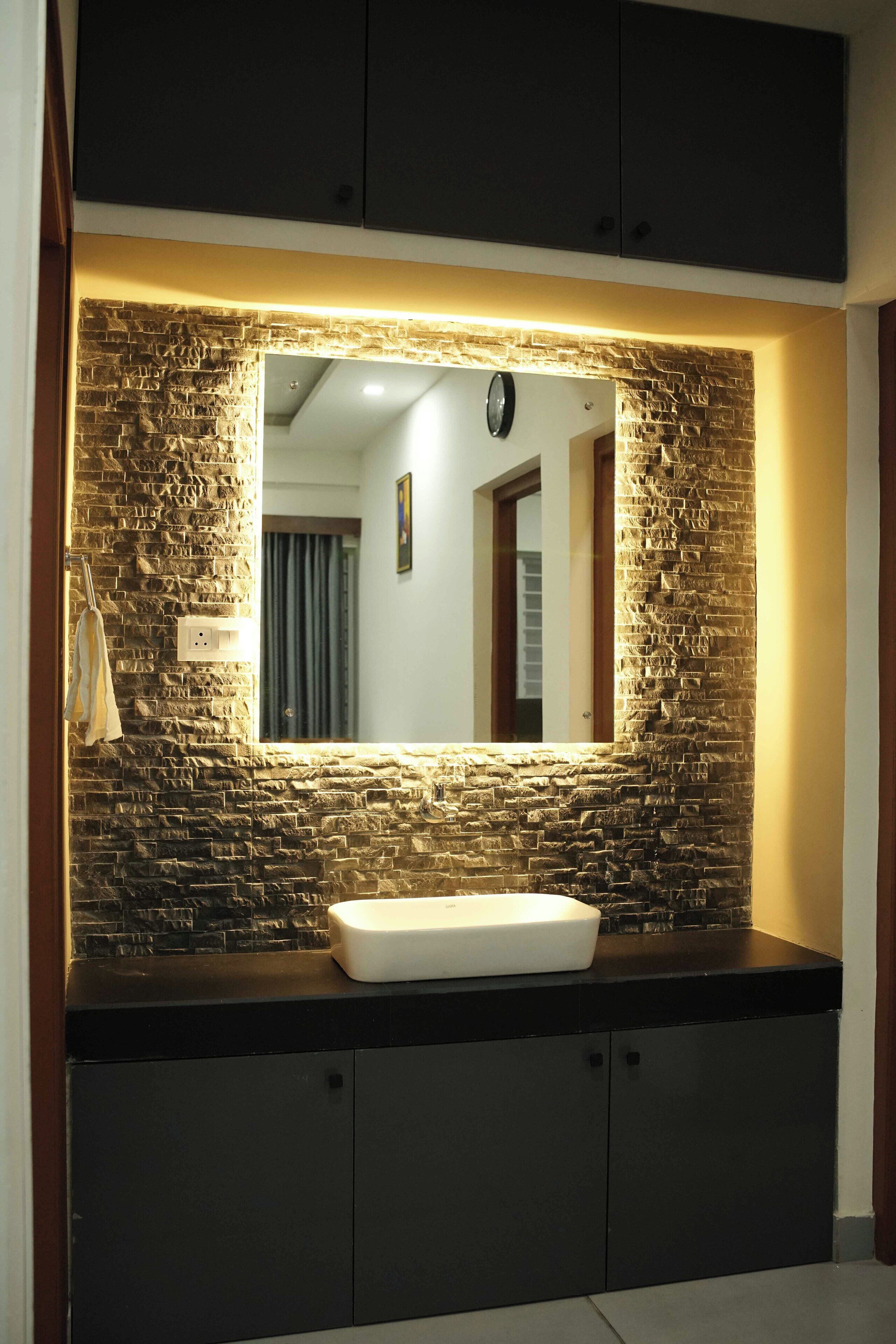 A bathroom with a stone wall, a white sink, and dark cabinets.